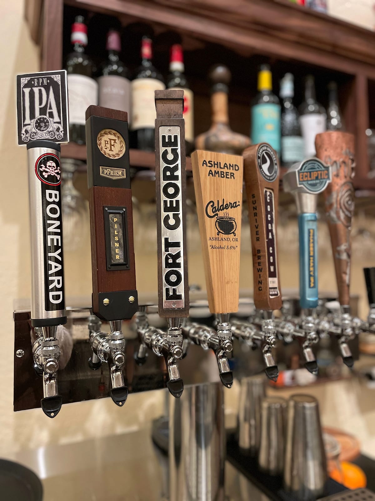 A row of beer tap handles with wine bottles behind