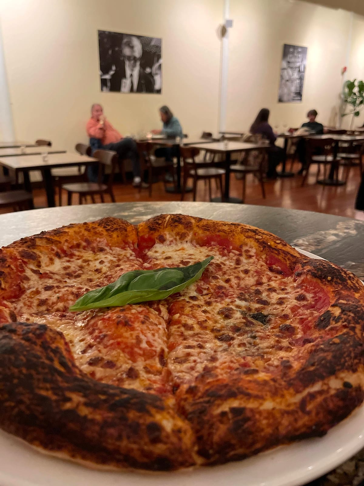 A margherita pizza with fresh basil, diners seated in the dining room behind